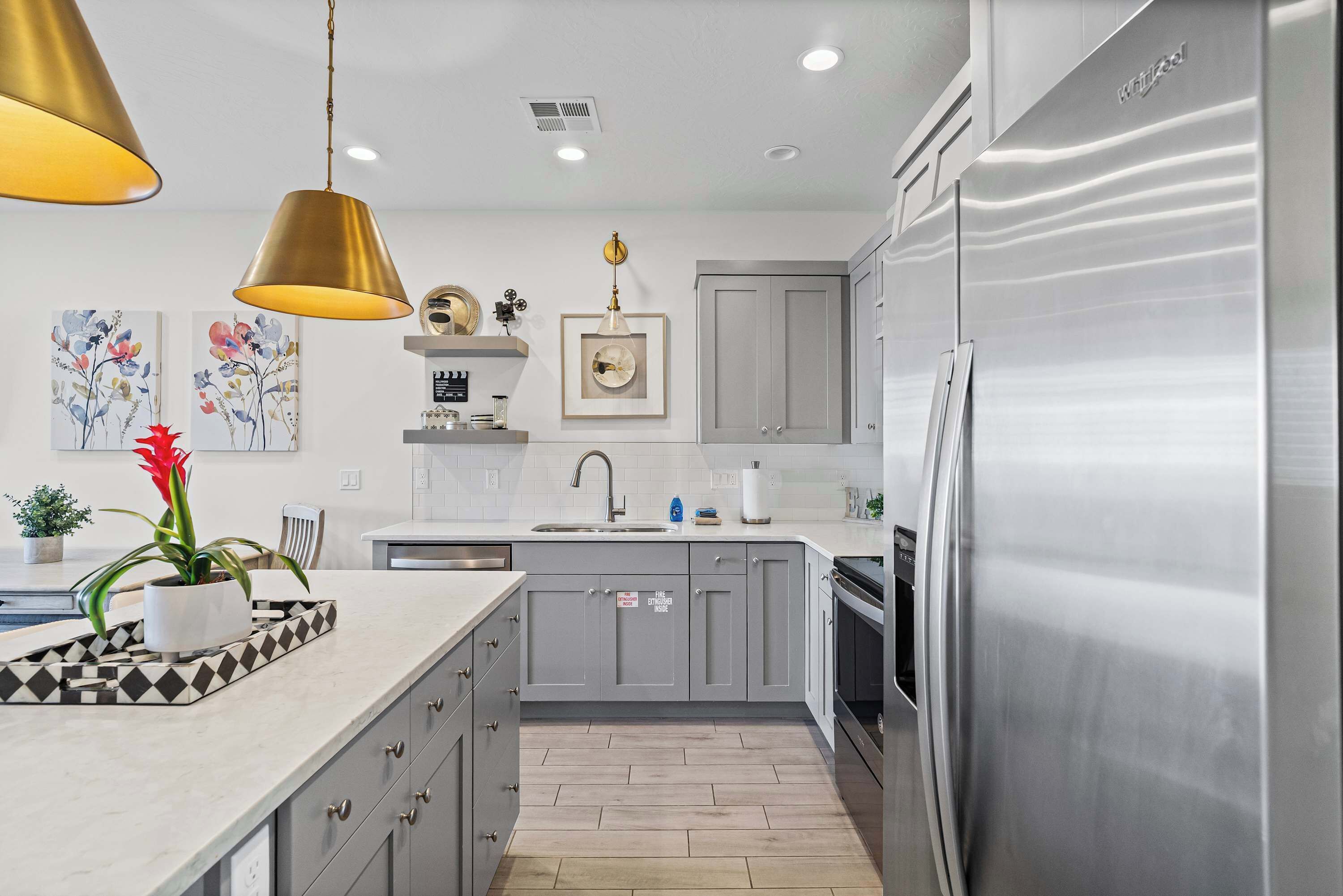 A modern kitchen with grey cabinets, stainless steel appliances, and pendant lighting.
