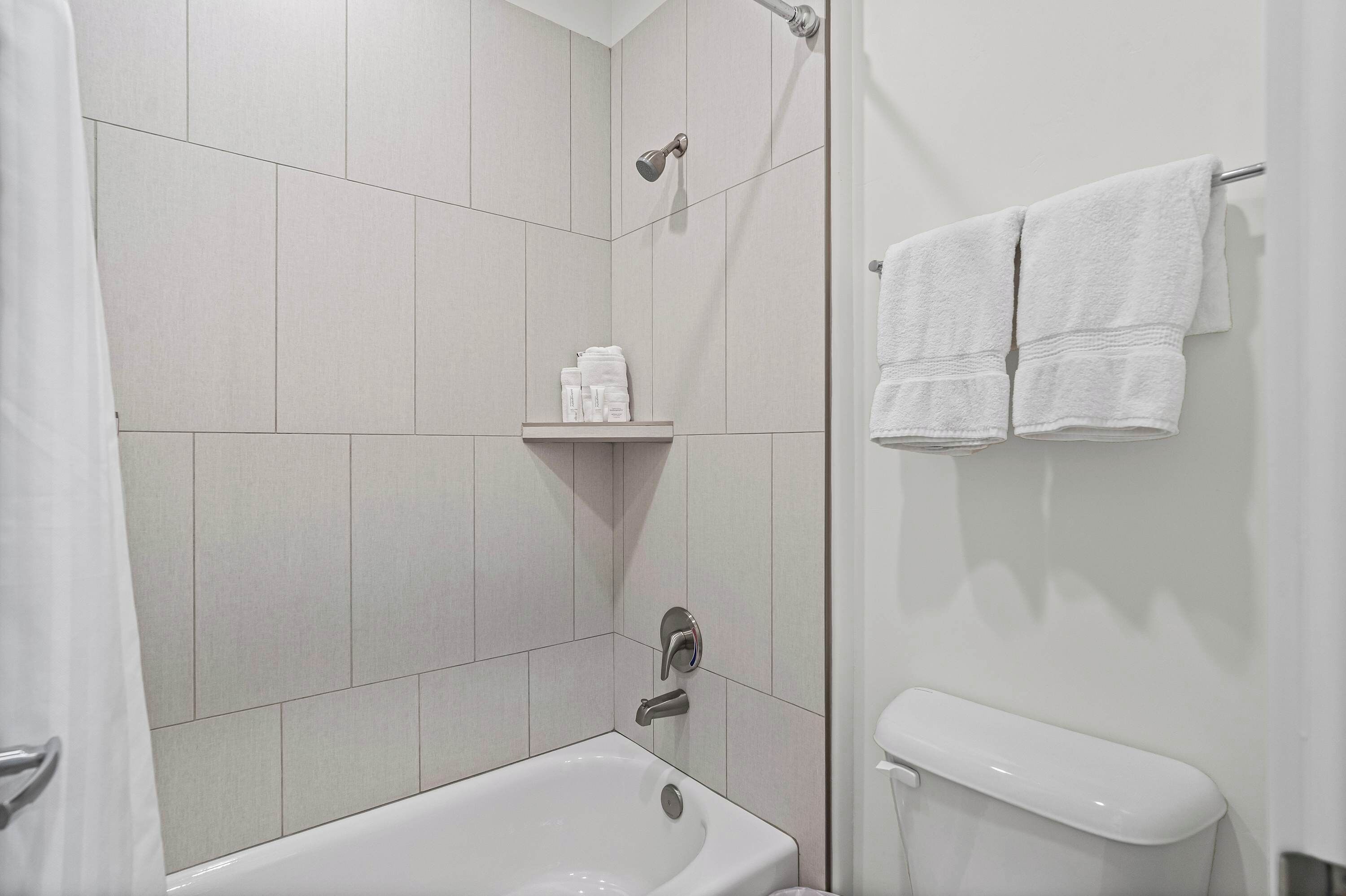 Une salle de bain moderne avec une baignoire, une douche et des toilettes. Deux serviettes sont accrochées au mur.