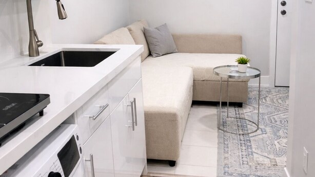 A compact kitchen with a built-in washing machine, a sink, and a small round table with a plant. - Sudio Basement Suite with Double Bed and kitchen, Entrance from Garage -Sleeps 2 (Milton)
