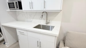 A modern kitchen with white cabinetry, a stainless steel sink, and a microwave. - Sudio Basement Suite with Double Bed and kitchen, Entrance from Garage -Sleeps 2 (Milton)