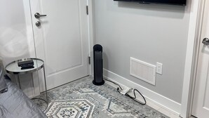 A bedroom with a bed, a small round table, a standing heater, a TV mounted on the wall, and a patterned rug. - Sudio Basement Suite with Double Bed and kitchen, Entrance from Garage -Sleeps 2 (Milton)