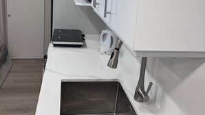 A modern kitchen with a stainless steel sink, white cabinetry, and a built-in coffee maker. - Sudio Basement Suite with Double Bed and kitchen, Entrance from Garage -Sleeps 2 (Milton)