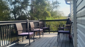 A deck with outdoor furniture, including chairs and a table, and a view of trees and a building in the background.