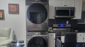 A compact kitchen with stainless steel appliances, a dining area with a chair, and a sofa.