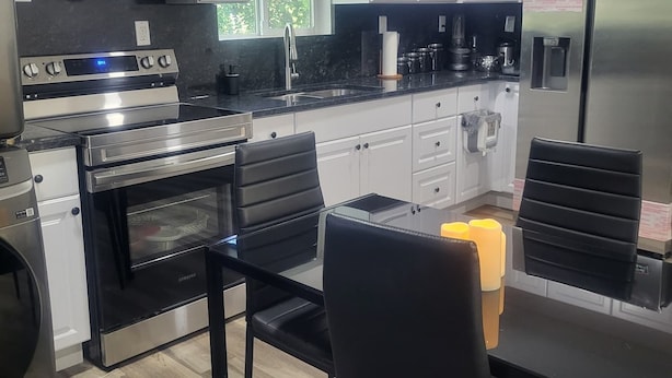 A modern kitchen with stainless steel appliances, white cabinetry, and a dining area with black chairs.