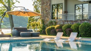 Ein Pool mit Liegestühlen, Sonnenschirm und einem Steinhaus im Hintergrund.