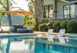 Ein Pool mit Liegestühlen, Sonnenschirm und einem Steinhaus im Hintergrund.