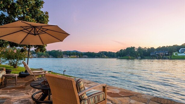Eine Terrasse mit Korbmöbeln und einem großen Sonnenschirm mit Blick auf einen See.