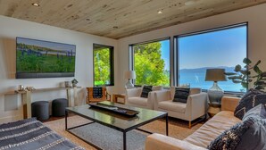 Amplia sala de estar con un gran ventanal que ofrece vistas al mar, techo de madera y un moderno conjunto de sofás.