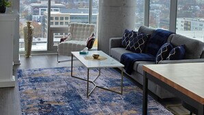 A modern living room with a large window, a sofa, a coffee table, and a rug. - Luxe 1-Bed Corner Suite in Music Row Nashville - Coworking, Gym, Skyline Views (Nashville)