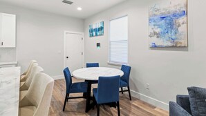 A modern dining area with a round table and blue chairs, a white door, and a large abstract painting on the wall. - New Build in Old West 3 Bed, 2 Bath Family Rental (Tampa)