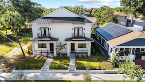 Une maison à deux étages avec un balcon au premier étage, des panneaux solaires sur le toit et un jardin bien entretenu à l’avant.