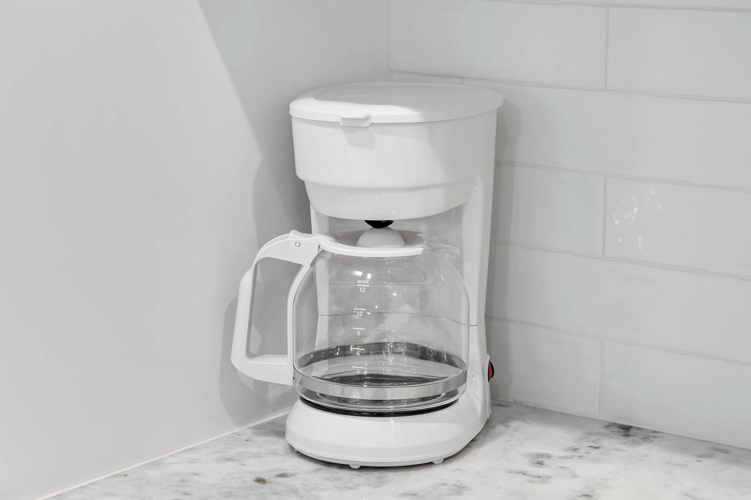 Une machine à café blanche, dotée d’une verseuse transparente et d’une échelle de mesure, posée sur un comptoir en marbre.