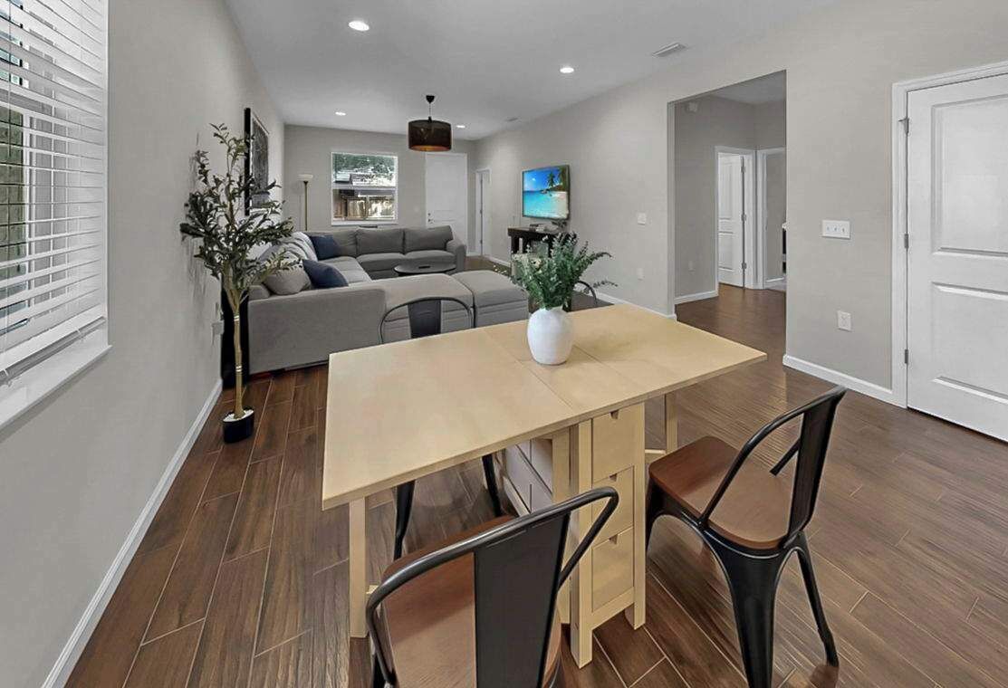 Un salon moderne avec un canapé, une table à manger et des chaises. Il y a un téléviseur accroché au mur et une plante sur la table.