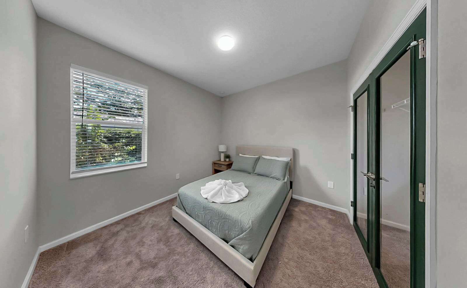 A bedroom with a single bed, a window with blinds, a nightstand, and a door.