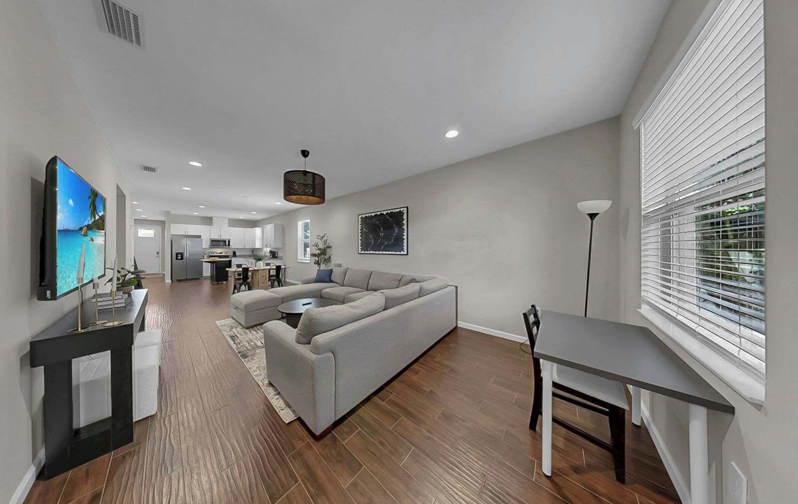 A modern living room with a grey sectional sofa, a dining table, and a TV mounted on the wall.