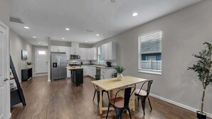 A modern kitchen with white cabinets, a central island, and a dining area with a table and chairs. - Cozy Downtown Tampa Retreat (Tampa)