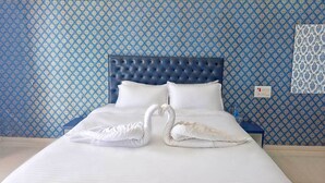 A hotel room with a blue patterned wallpaper, a tufted headboard, white bedding, and two swan-shaped towels on the bed. - Wilson Valley Resort (Dharampur)