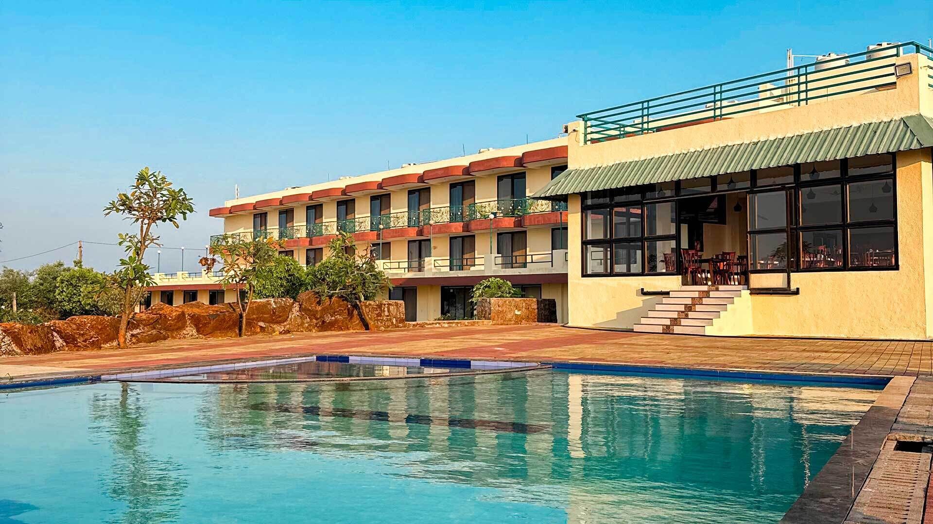 A hotel with a swimming pool, multiple balconies, and a flat roof.