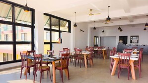 A spacious dining area with multiple tables and chairs, large windows, and ceiling fans. - Wilson Valley Resort (Dharampur)