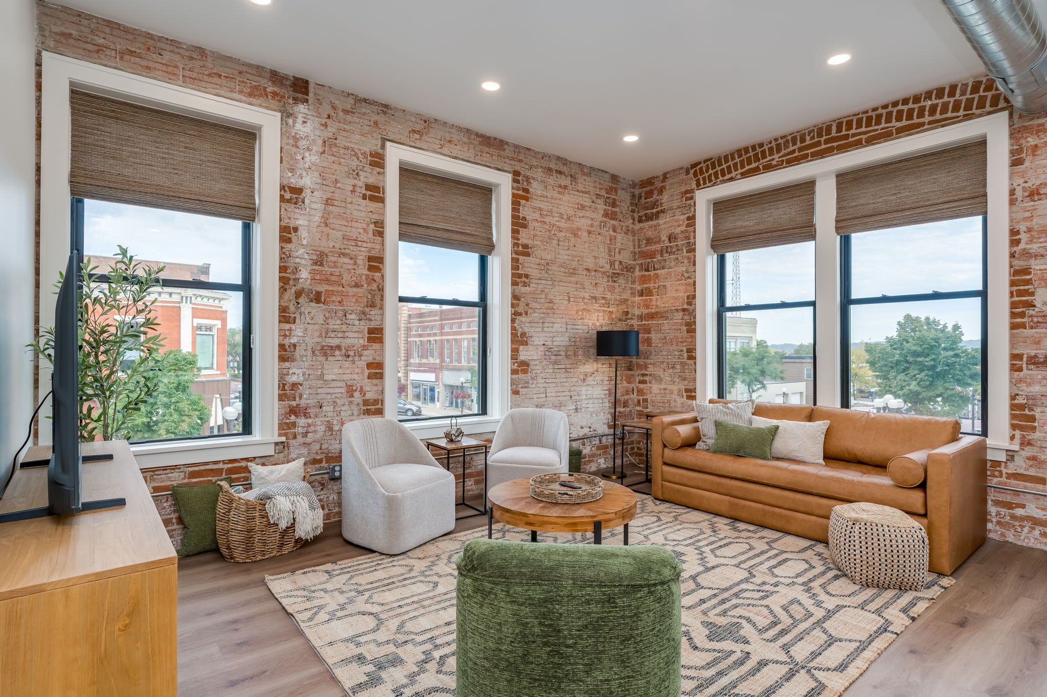A modern living room with brick walls, large windows, a leather sofa, and a wooden coffee table.