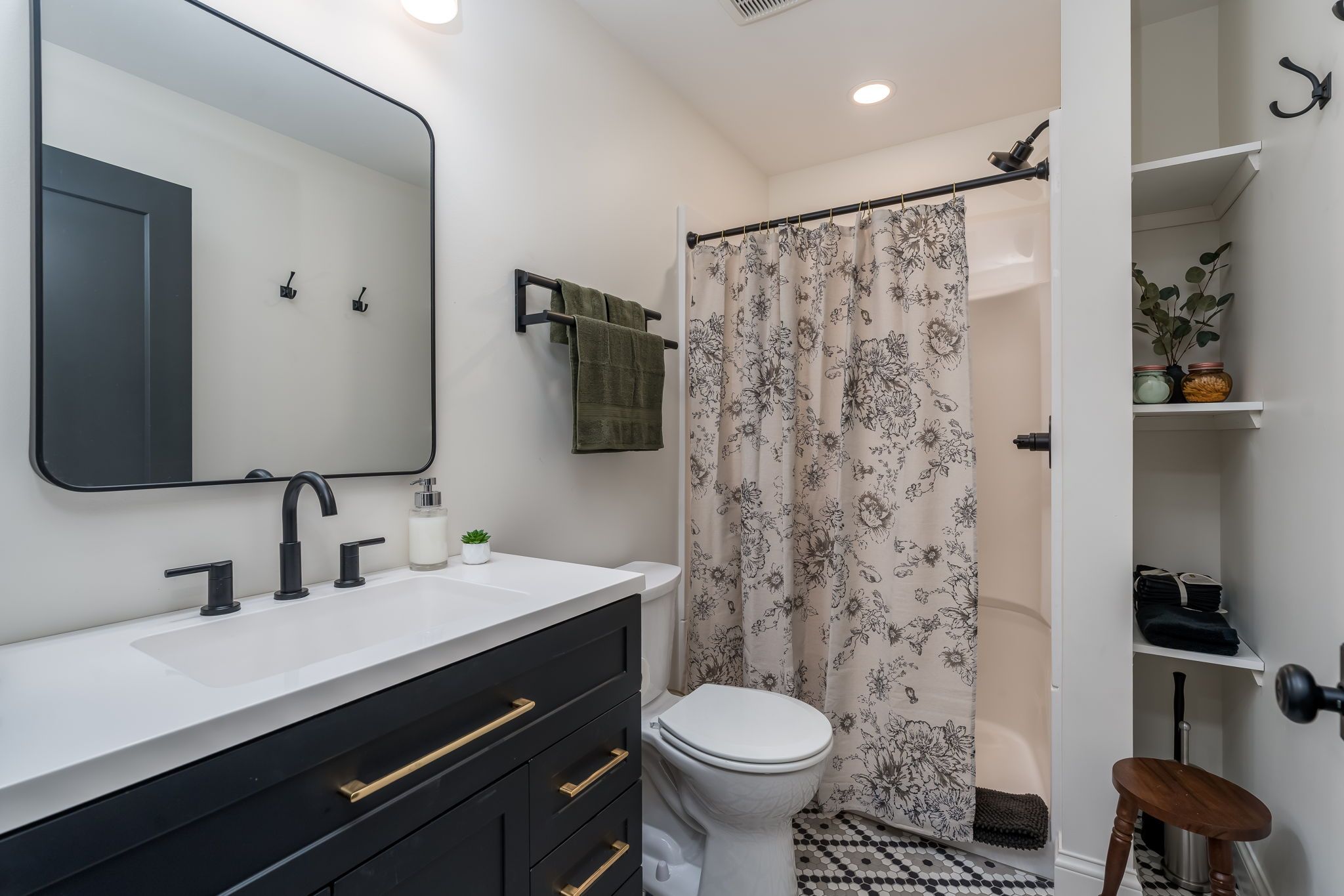 A bathroom with a white sink, black cabinet, and a toilet. There is a shower curtain with a floral pattern.