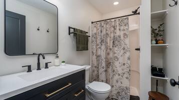 A bathroom with a white sink, black cabinet, and a toilet. There is a shower curtain with a floral pattern.