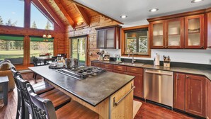 A modern kitchen with wooden cabinetry, a central island, and large windows. - McCall A-Frame on Golf Course, 5 Minutes from Town + Huge Yard, Hot Tub & 7 Beds (McCall)