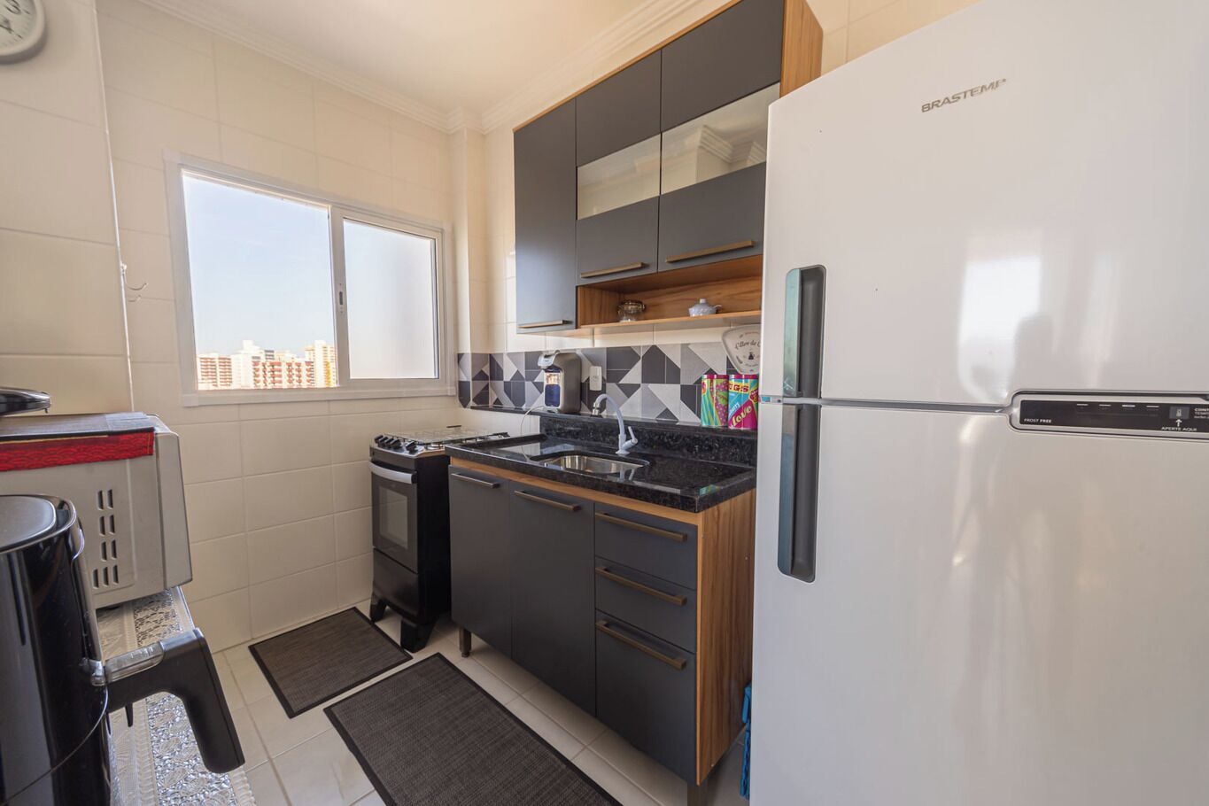 A compact kitchen with a gas stove, a built-in oven, a refrigerator, and a window providing a view of the cityscape.