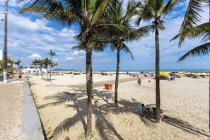 A beach with palm trees, a sandy shore, and beach umbrellas. - Apto com Ar e 2 Dorm na Vila Mirim Perto da Praia (Praia Grande)