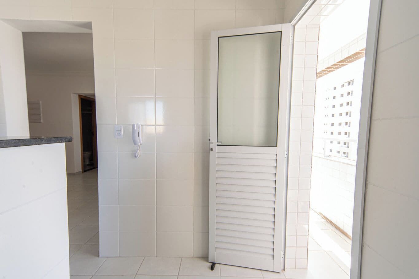 A white tiled bathroom with a shower door, a towel rack, and a toilet visible in the background.
