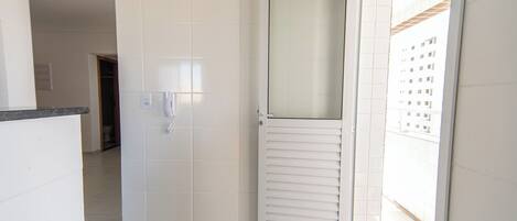 A white tiled bathroom with a shower door, a towel rack, and a toilet visible in the background.