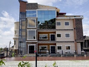 A multi-story residential building with a modern design, featuring a mix of stone and glass facades, multiple balconies, and a gated entrance. - Quads Villa (Accra)