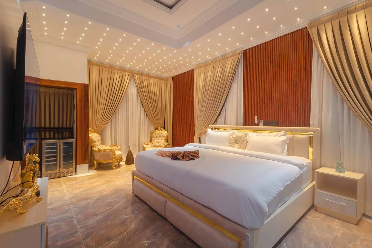 A spacious bedroom with a large bed, a golden statue, a TV, and a modern ceiling design.