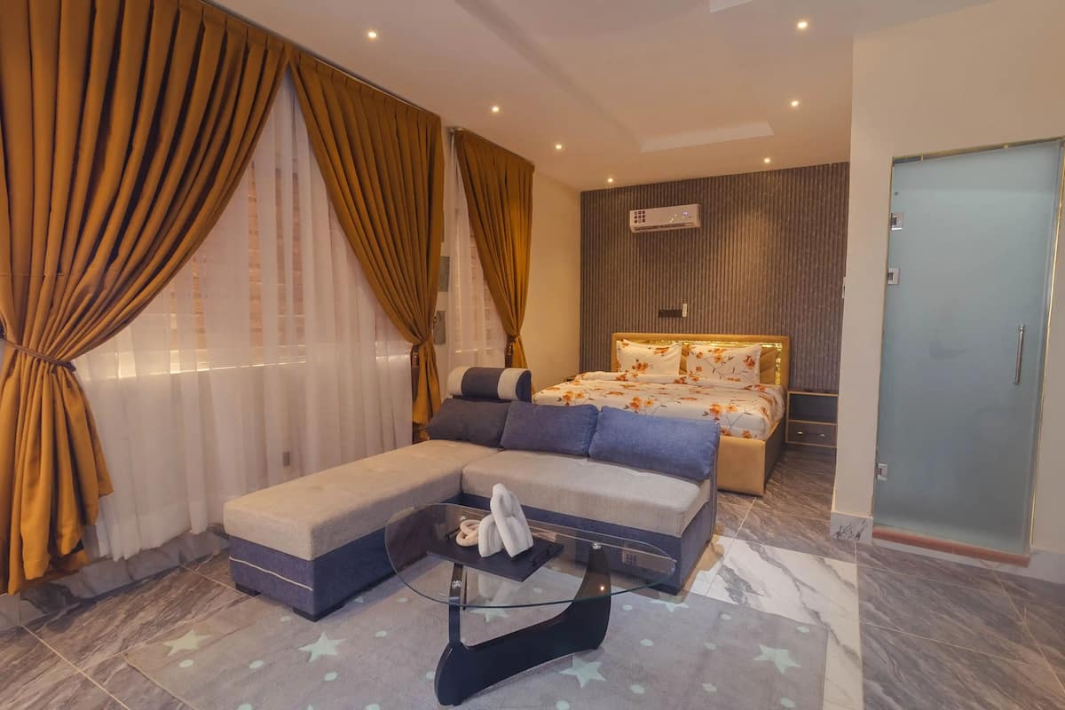 A modern hotel room with a large sofa, a glass coffee table, and a bed with floral bedding.
