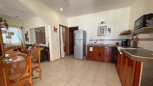 A spacious kitchen with wooden cabinets, a refrigerator, and a microwave. There is a dining area with a wooden chair and a table. - MARAVILLA: Spacious 1-bedroom apartment with AC in charming Celestún. (Celestún)