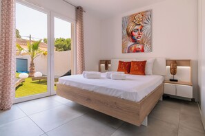 A modern bedroom with a large bed, a painting on the wall, and a view of the outside. - Duo Villas – 6BR, 2 Pools, Beach 500 m (Sérignan)