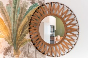 A round mirror with a leaf pattern, reflecting a kitchen area with a refrigerator, microwave, and a kettle on the counter. - Duo Villas – 6BR, 2 Pools, Beach 500 m (Sérignan)