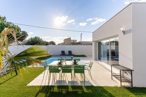 A modern outdoor patio with a pool, green chairs, and a glass door leading to a building. - Duo Villas – 6BR, 2 Pools, Beach 500 m (Sérignan)