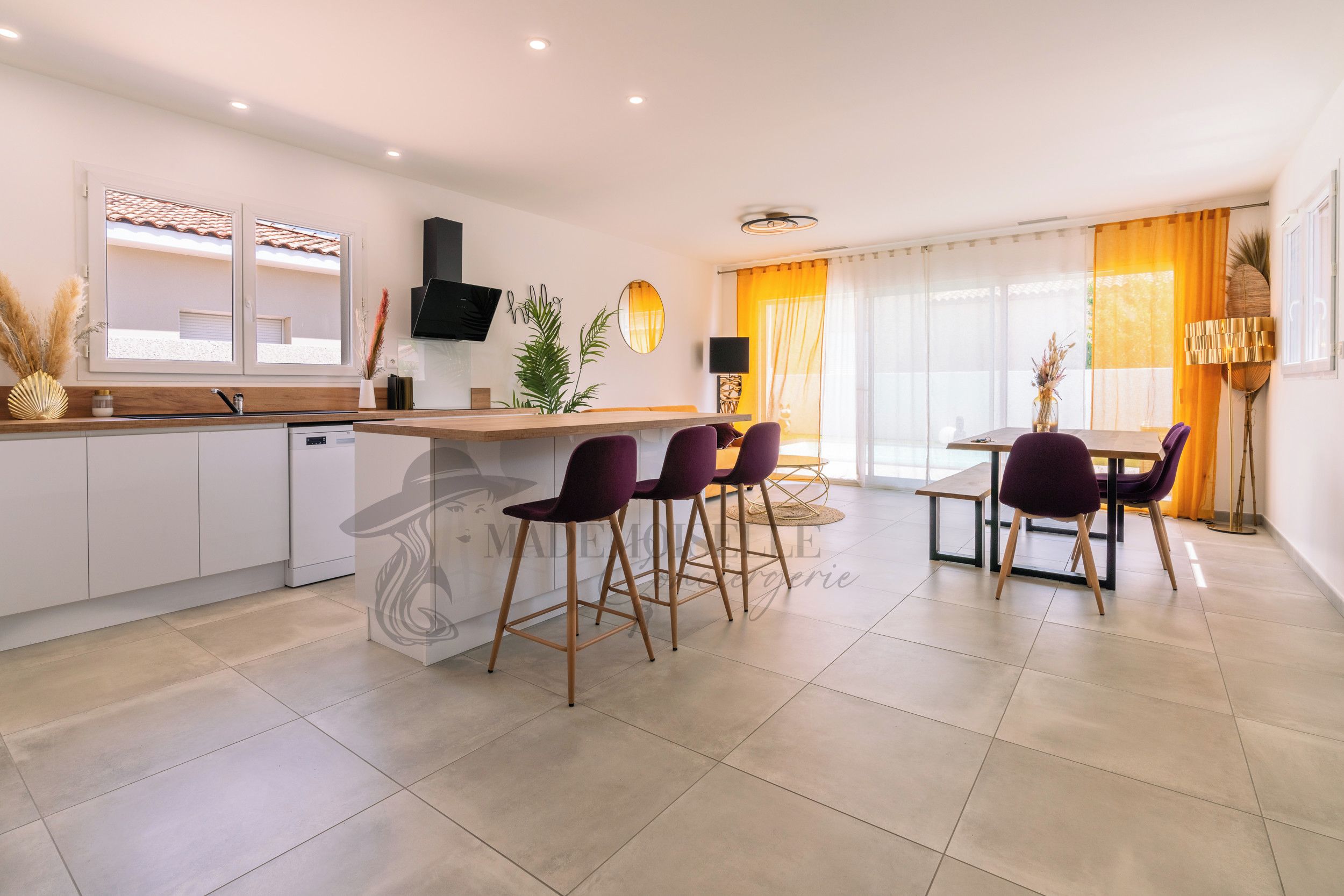 A modern kitchen with a bar area, dining space, and a large window with curtains.