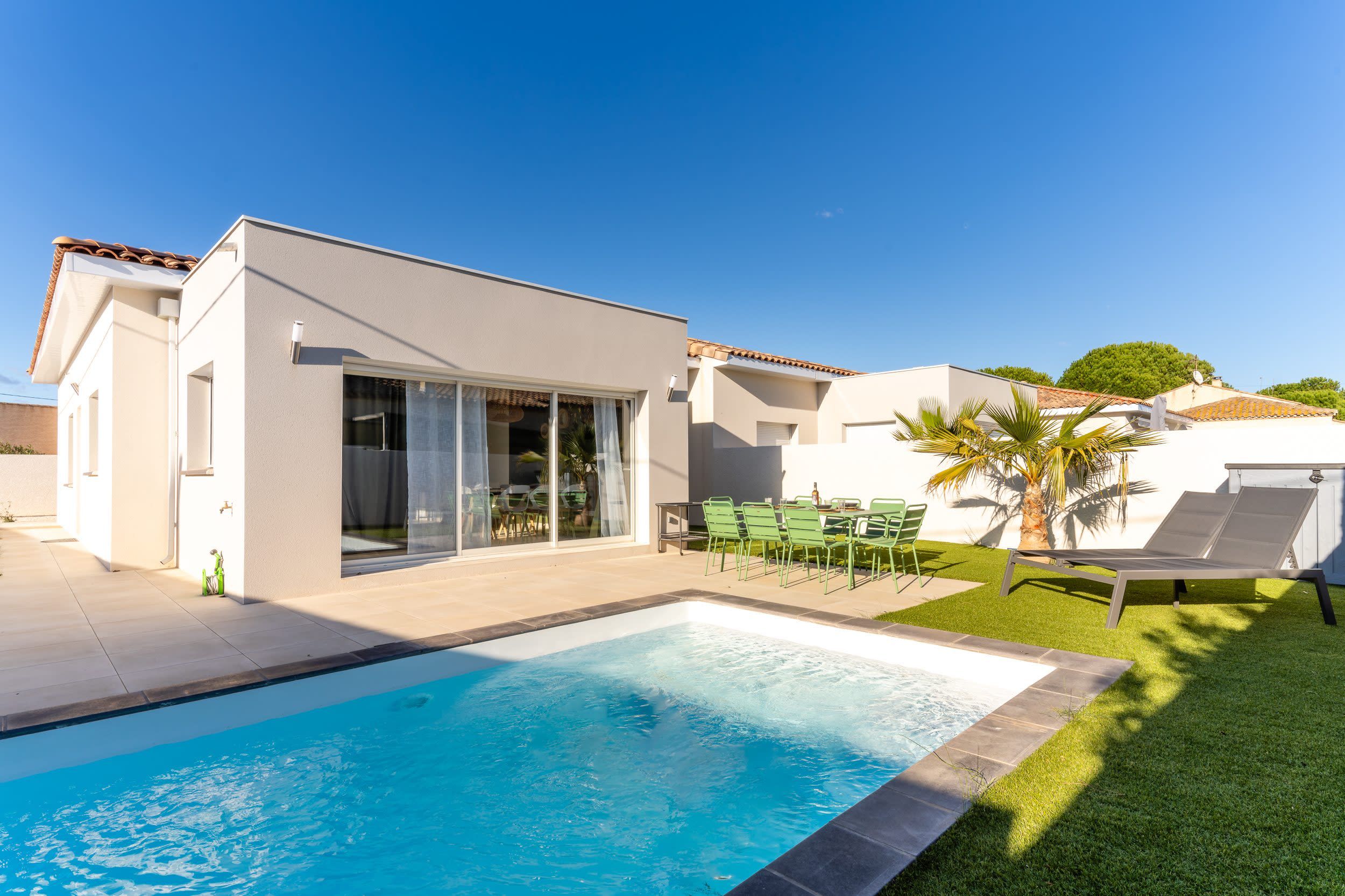 Ein modernes Haus mit Swimmingpool, Terrasse mit Stühlen und Rasenfläche.