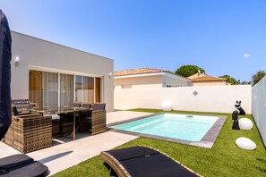 A modern outdoor pool area with a lounge chair, a table with chairs, and a small statue. - Duo Villas – 6BR, 2 Pools, Beach 500 m (Sérignan)