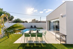 A modern outdoor patio with a pool, green chairs, and a glass door leading to a poolside area. - Duo Villas – 6BR, 2 Pools, Beach 500 m (Sérignan)