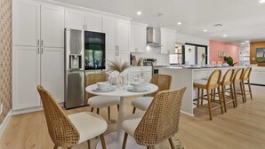 A modern kitchen with white cabinetry, a dining area with wicker chairs, and a central island. - Family Fun Oasis: Heated Pool, Pickleball, Basketball, Mini Golf & Game Room (Clearwater)