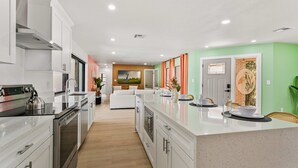 A modern kitchen with stainless steel appliances, a large island, and a dining area with a view of the outdoors. - Family Fun Oasis: Heated Pool, Pickleball, Basketball, Mini Golf & Game Room (Clearwater)