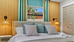 A neatly made bed with a headboard, two wall-mounted lamps, and a view of the outdoors through a window. - Family Fun Oasis: Heated Pool, Pickleball, Basketball, Mini Golf & Game Room (Clearwater)