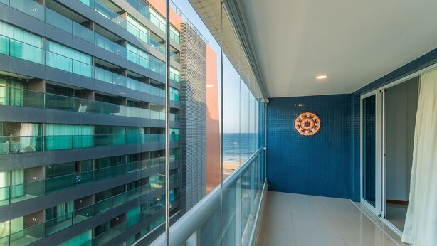 A balcony with a glass railing overlooking a cityscape and a beach. - Your Exclusive Stay in a Building With a Pool Just Steps From the sea - WJA (Salvador)