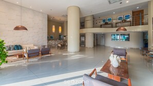 A spacious lobby with a high ceiling, a central column, and a seating area with sofas and chairs. - Your Exclusive Stay in a Building With a Pool Just Steps From the sea - WJA (Salvador)