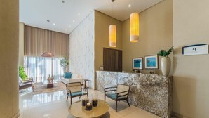 A modern lobby with a reception desk, seating area, and a large window with curtains. - Your Exclusive Stay in a Building With a Pool Just Steps From the sea - WJA (Salvador)