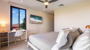 A bedroom with a bed, desk, chair, ceiling fan, and a painting.